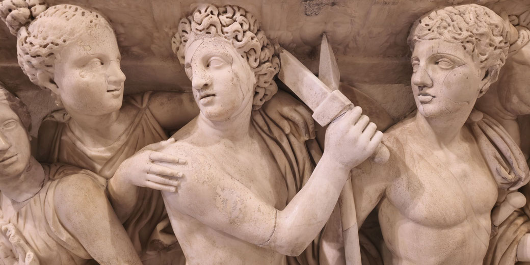 Marble relief of a central figure holding a sword, flanked by others with expressive faces, suggesting tension or drama.