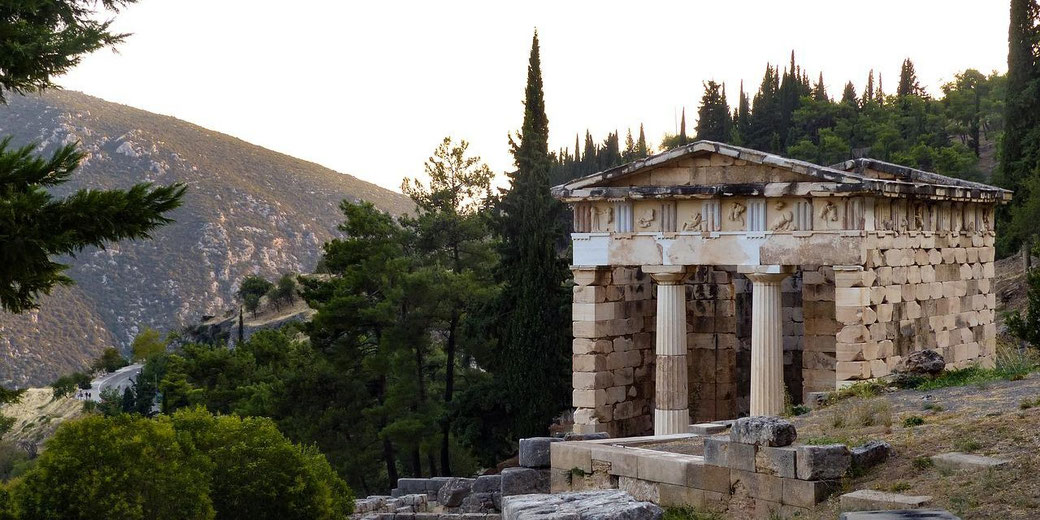 Ancient stone temple with Doric columns sits among trees and hills, partially lit by the setting sun.