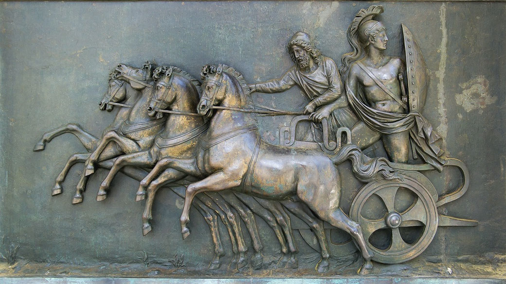 Bronze relief sculpture showing four horses pulling a chariot with two armored male figures, one steering and the other holding a shield.