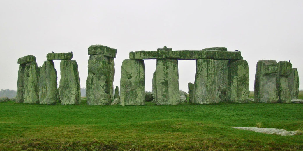 Stonehenge, an iconic prehistoric monument in England, featuring large standing stones arranged in a circular layout, set against a grassy landscape under an overcast sky.