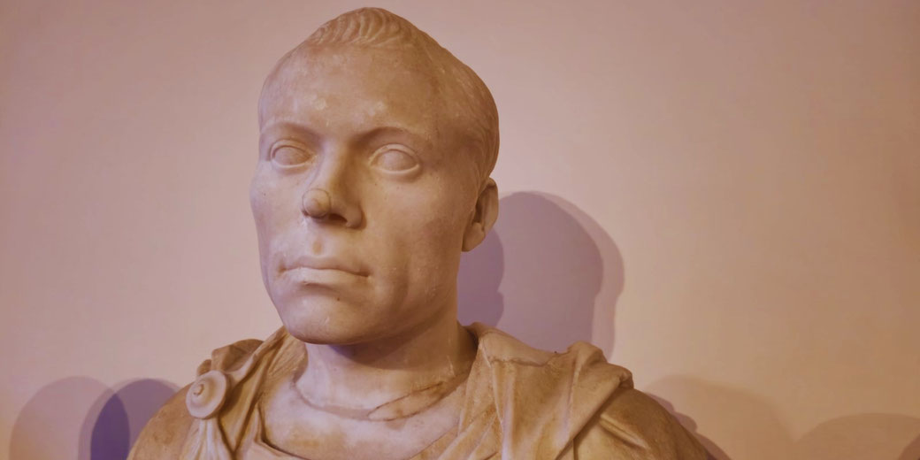 Marble bust of a young man with short, combed hair and a calm expression, wearing a draped garment fastened with a brooch on the shoulder.