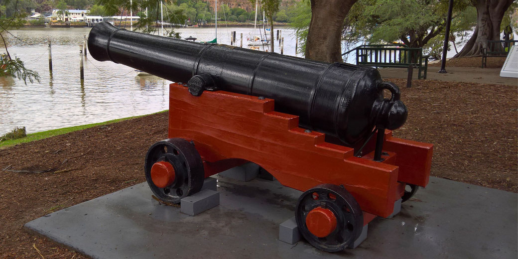 A restored colonial-era cannon mounted on a red wooden carriage, displayed outdoors near a waterfront. It serves as a historical monument, likely commemorating maritime defense.
