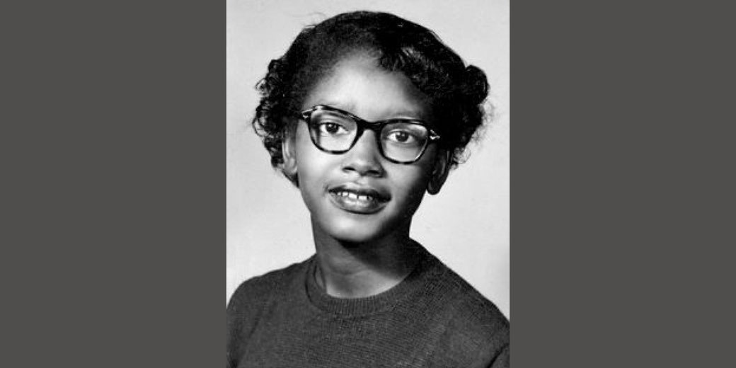 A black-and-white portrait of a young girl wearing glasses and a sweater, looking slightly off-camera with a calm expression.