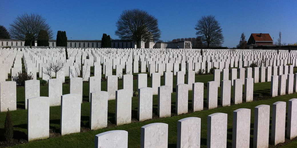A vast military cemetery with rows of white gravestones stretching across a manicured green lawn under a clear blue sky.