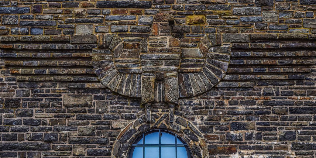 Stone eagle relief built into a brick wall above an arched window with blue glass panes.
