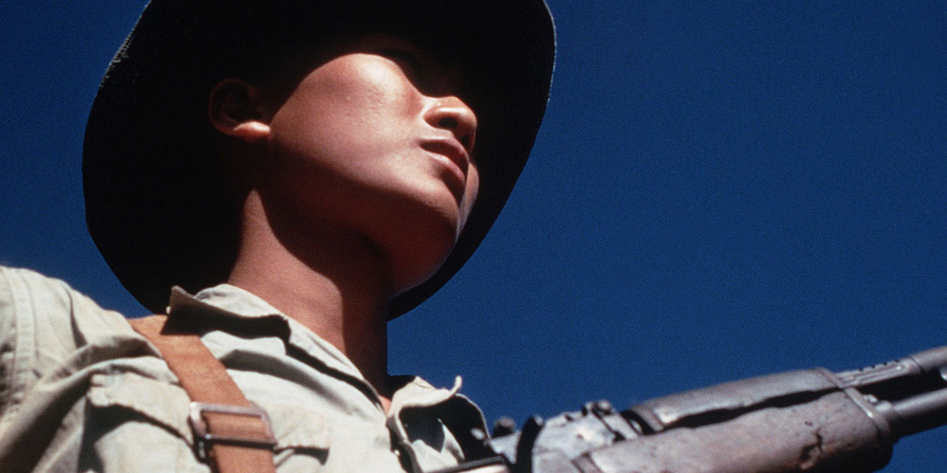 Viet Cong soldier stands beneath a Viet Cong flag carrying his AK-47 rifle. He was participating in the exchange of POWs by the Four Power Joint Military Commission