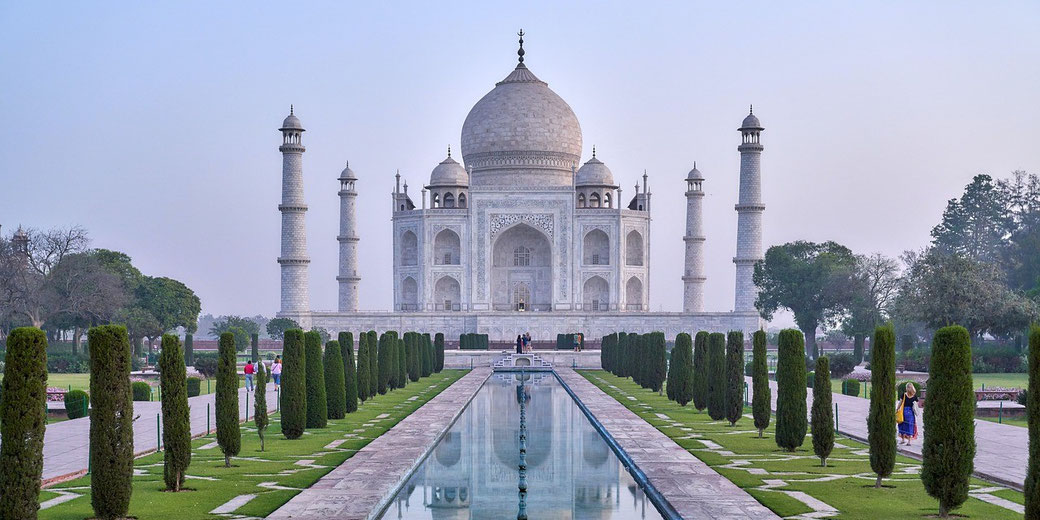 The Taj Mahal stands symmetrically with its white marble dome and four minarets, fronted by a long pool and garden path.