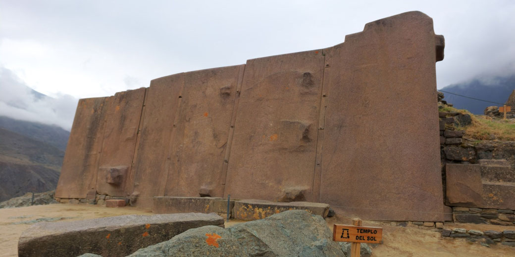 The Temple of the Sun at Ollantaytambo, Peru. It features massive Inca stone walls with precise fitting, set against a mountainous backdrop with misty clouds.