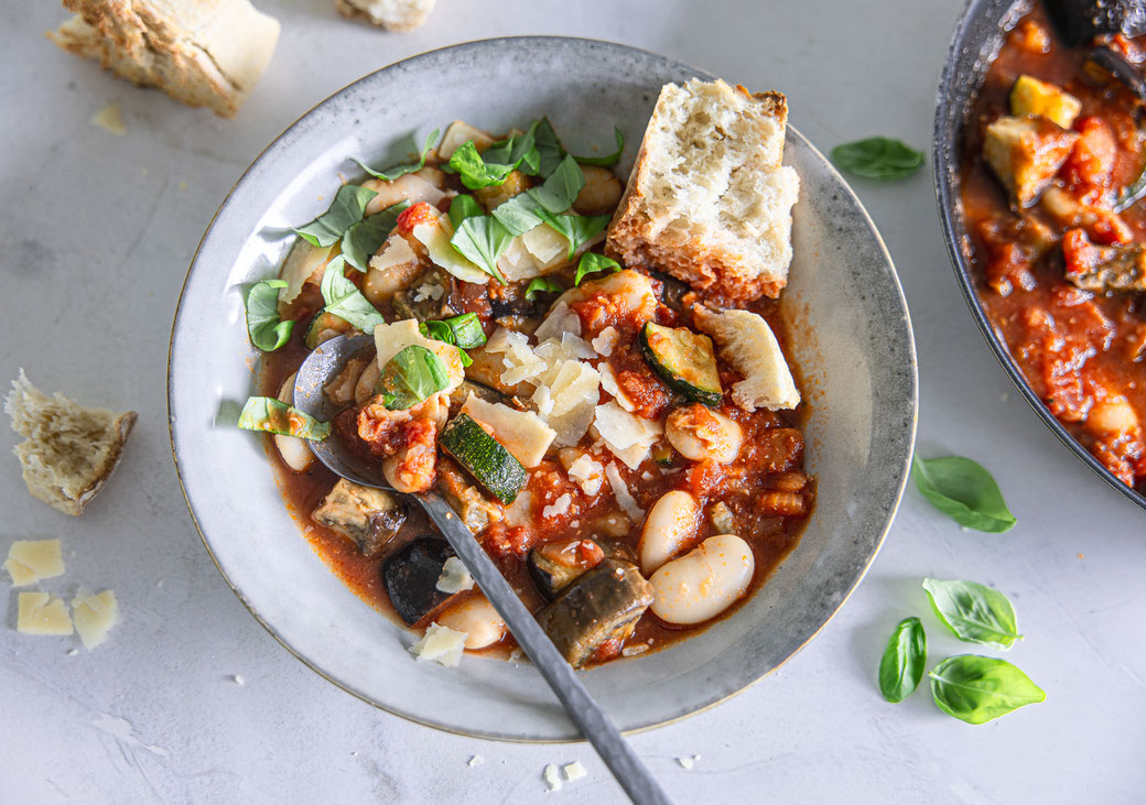 Toskanisches Gemüse-Ragout mit Aubergine, Zucchini, weißen Bohnen und Parmesan, serviert mit frischem Basilikum und knusprigem Baguette