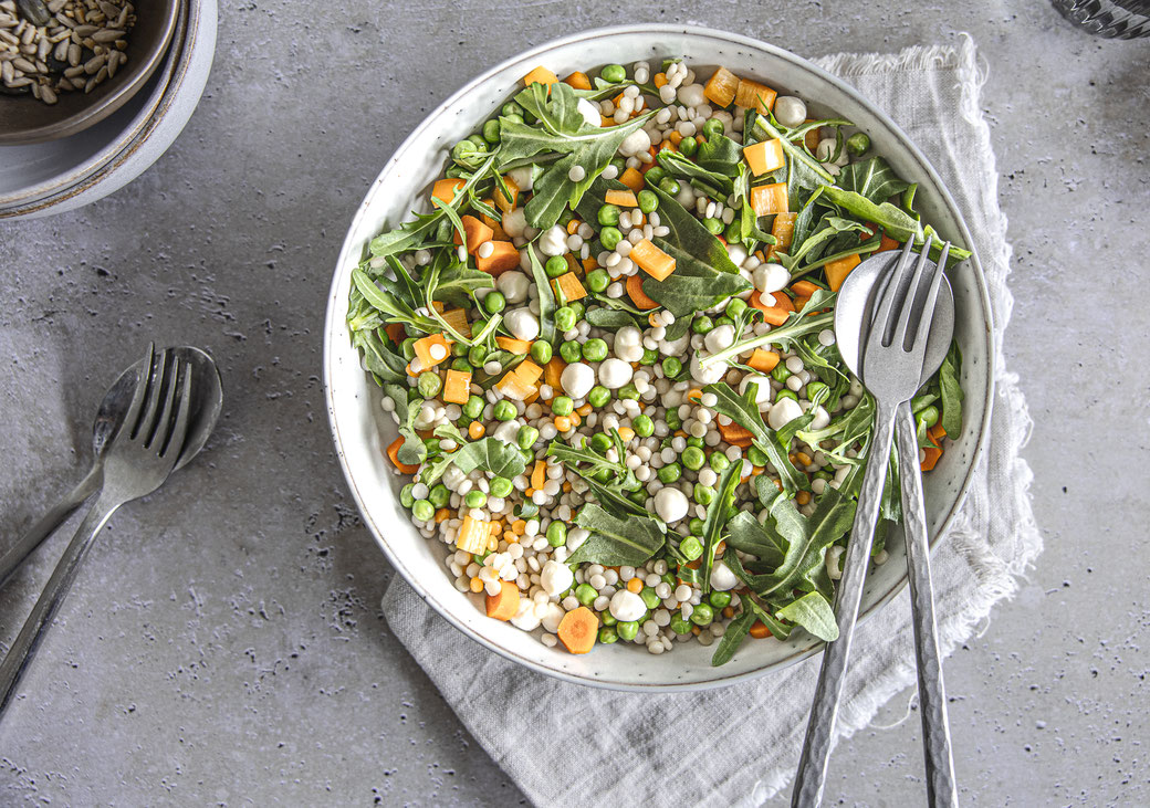 Herbstlicher Pearl-Couscous-Salat mit Mozzarella, Rucola und Gemüse in einer Schüssel serviert.