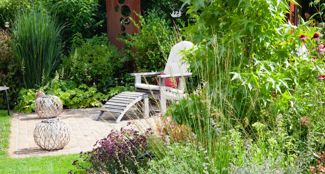 Ein Liegestuhl steht auf einer gepflasterten Fläche inmitten von üppiger Bepflanzung 