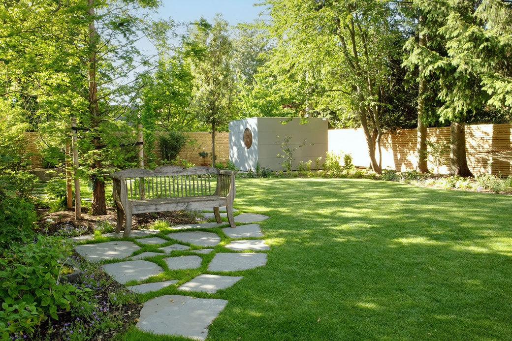 Eine Holzbank unter Bäumen und Sträuchern wird zum schattigen Sitzplatz