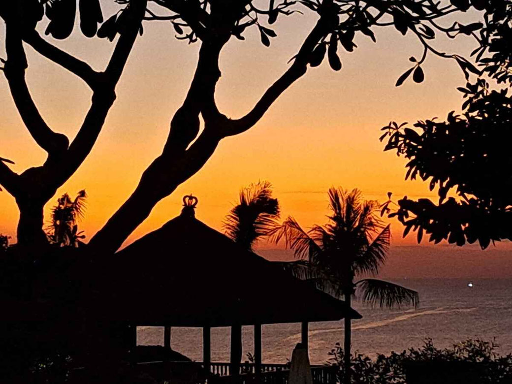 Goldener Sonnenuntergang über dem Meer mit Palmensilhouetten und einer Gazebo im Ayana Resort.
