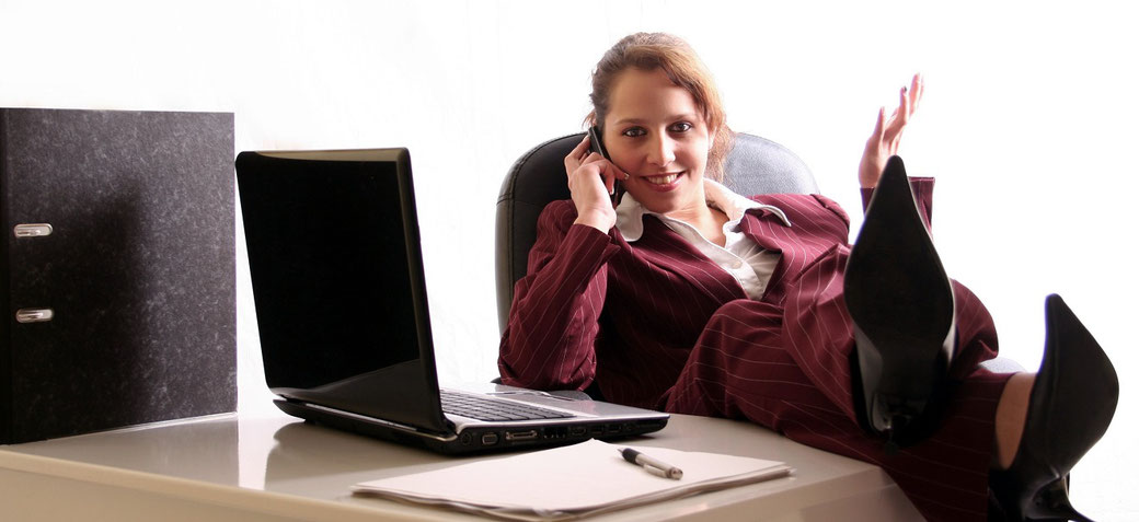 Frau mit Laptop auf dem Tisch und Telefon in der Hand beim Umbuchen einer Seminar-Versicherung