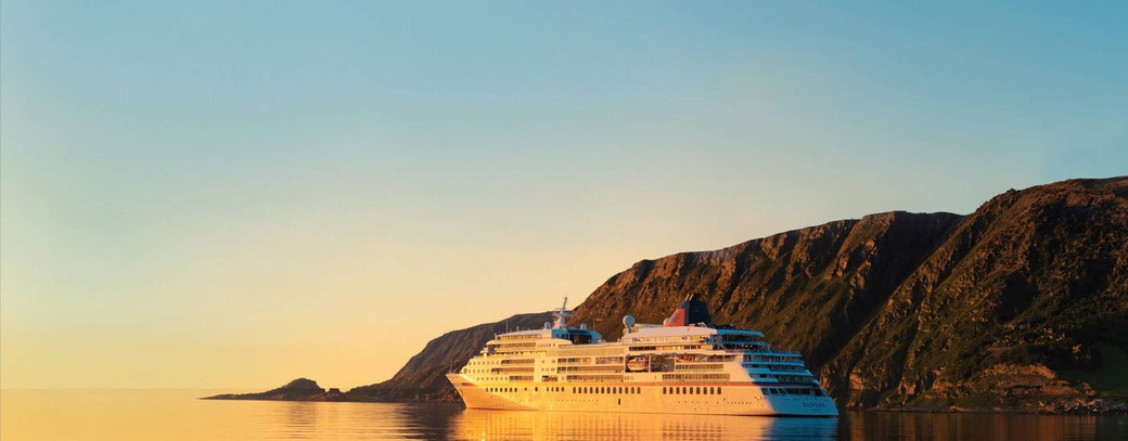 Kreuzfahrtschiff vor einer dramatischen Fjordlandschaft im warmen Licht der Mitternachtssonne
