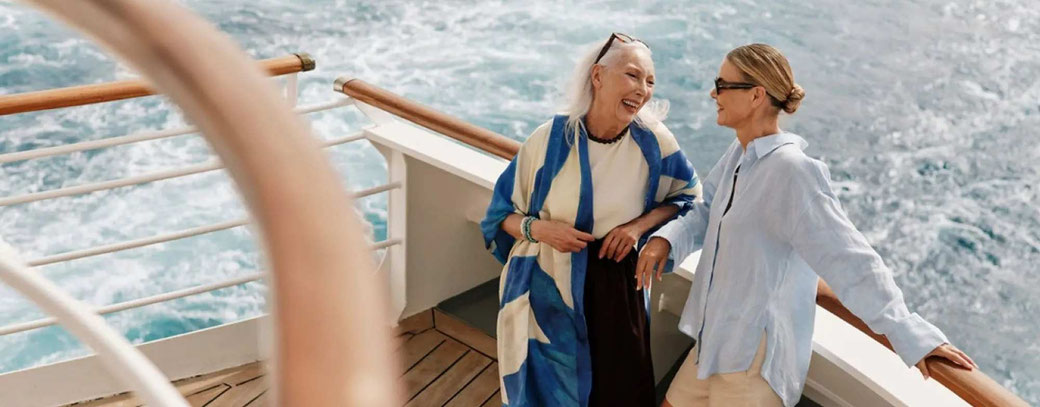 Zwei Damen unterhalten sich fröhlich an Deck eines Kreuzfahrtschiffes.