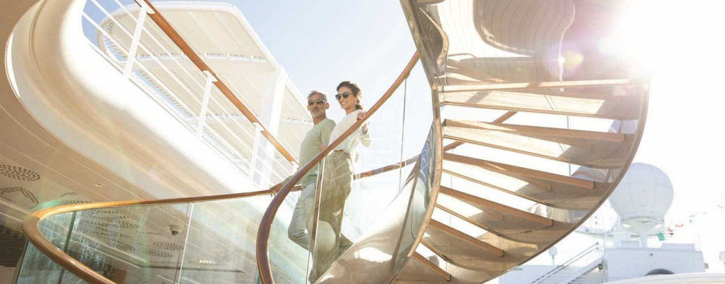 Gästepaar steigt an Bord der Seven Sea Grandeur eine Wendeltreppe unter offenem Himmel hinab