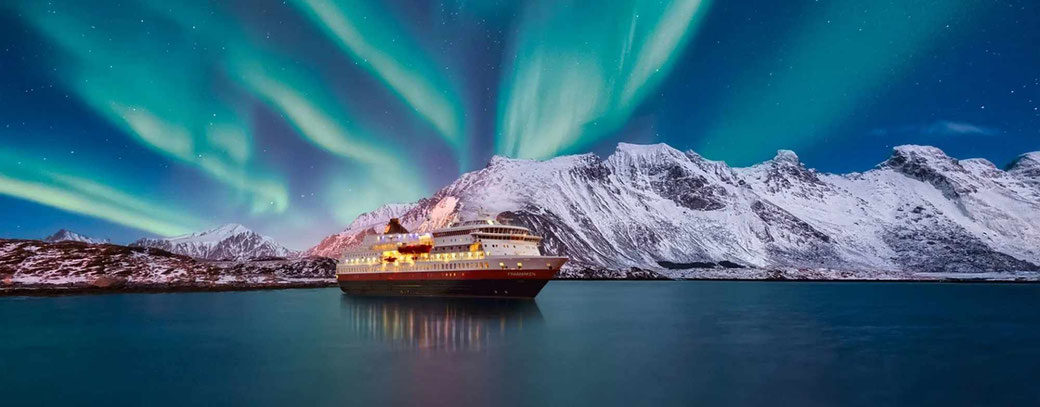 Das Hurtigruten Schiff MS Finnmarken vor einer Bucht im Polarlicht und schneebedeckten Bergen
