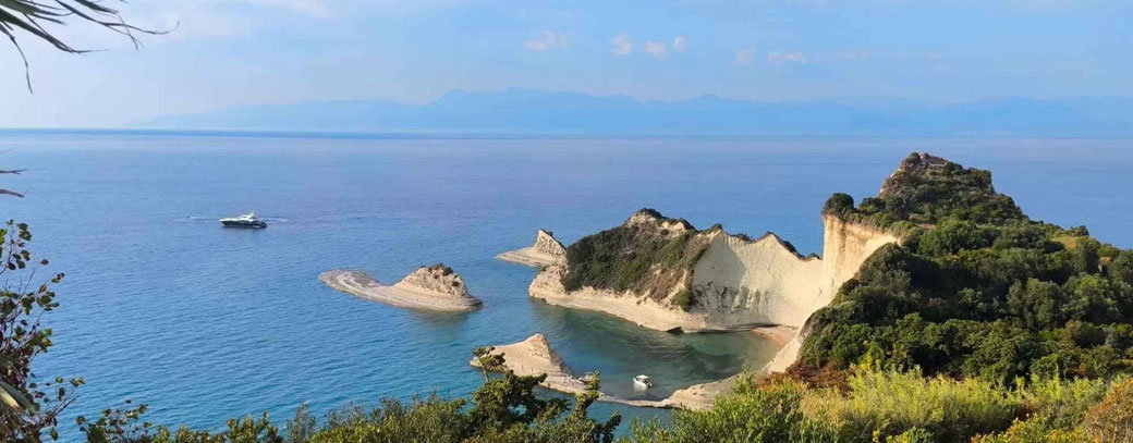 Küstenlandschaft mit türkisblauem Meer, weißen Felsformationen und Yacht vor Korfu in Griechenland