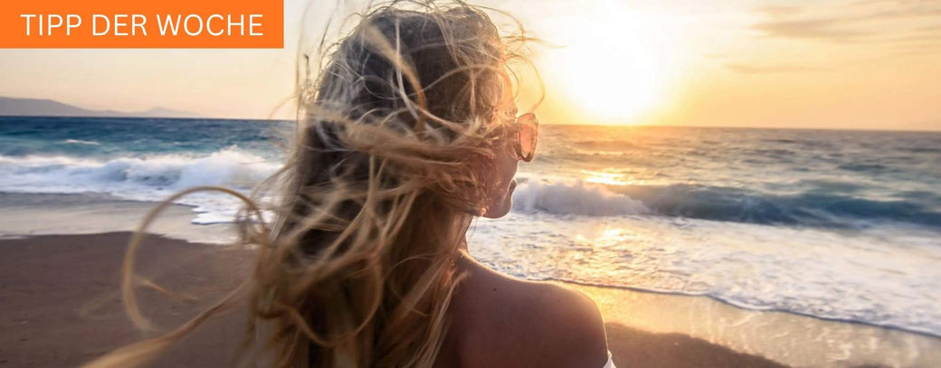 Frau blickt bei Sonnenuntergang auf das Meer