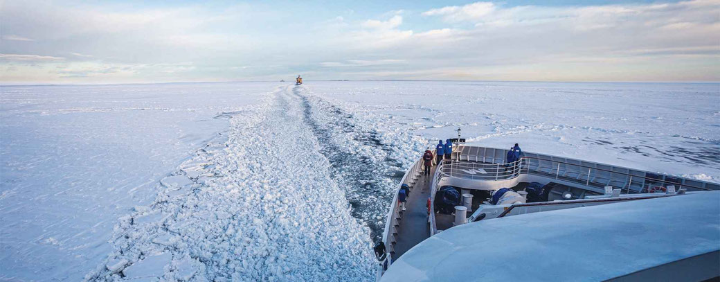 Bug der HANSEATIC nature fährt durch ein Eismeer. Gäste in blauen Expeditionsjacken an Deck blicken hinaus auf die Eislandschaft.
