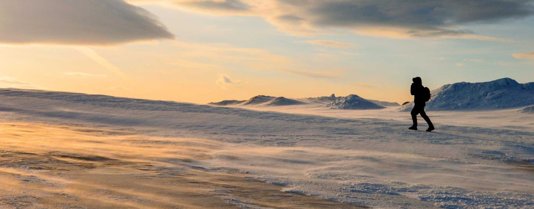 Aleinreisender wandert durch verschneite arktische Landschaft bei Sonnenuntergang