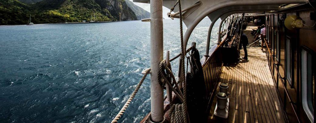 Blick vom Deck eines traditionellen Segelschiffs von SEA CLOUD auf eine beeindruckende Fjordlandschaft mit steilen, bewaldeten Berghängen und ruhigem Wasser