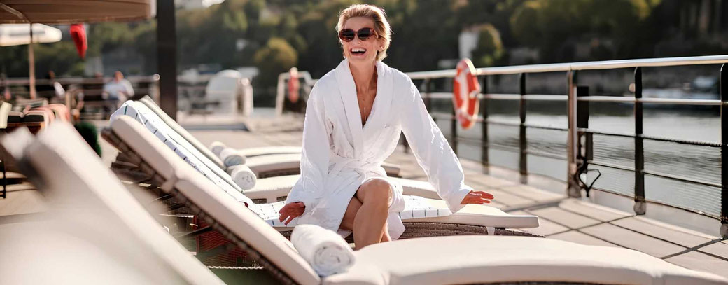 Ein weiblicher Gast im Bademantel auf einer Sonnenliege auf dem Oberdeck eines Riverside Luxury Cruises Schiff
