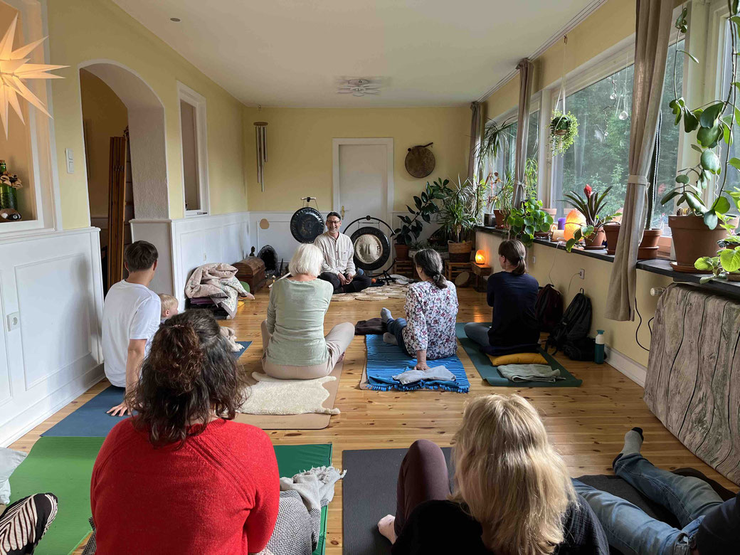 Martin Schmitz von KOMM RUNTER Hamburg sitzt vor mehreren Personen in einem Veranstaltungsraum vor seinen Gongs