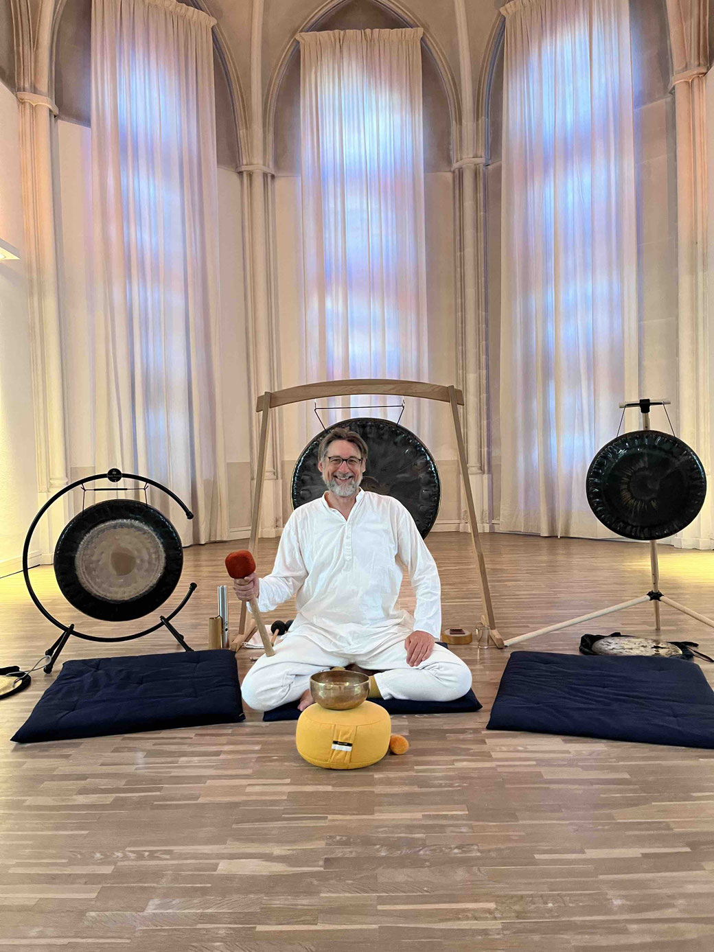 Martin Schmitz sitzt vor seinem Gong in der Kirche der Stille und sieht glücklich aus