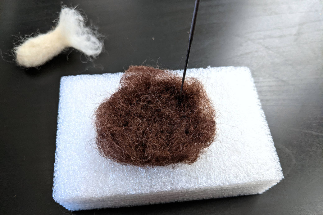 Brown wool on foam block, needle felted into round shape for mushroom cap, white stem in the background