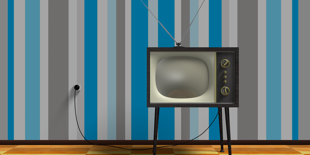 A retro television with antenna stands on wooden legs in front of a striped blue and gray wall.