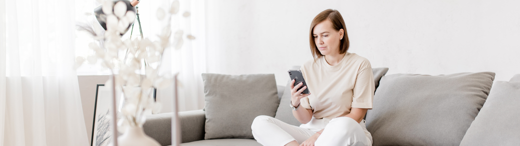 Frau sitzt auf dem Sofa, schaut auf ihr Smartphone