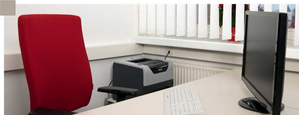 Ein freier roter Schreibtischstuhl am Schreibtisch mit Computer - Symbol für freie Arbeitsplätze