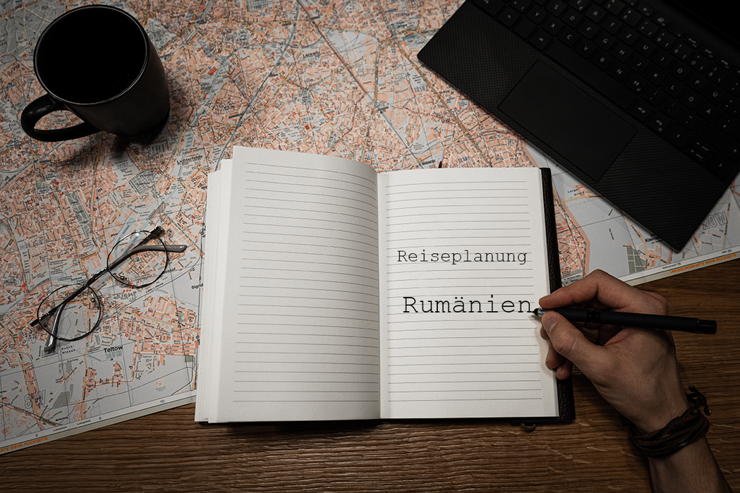 Ein Mann schreibt in ein Tagebuch den Begriff Reiseplanung Rumänien.