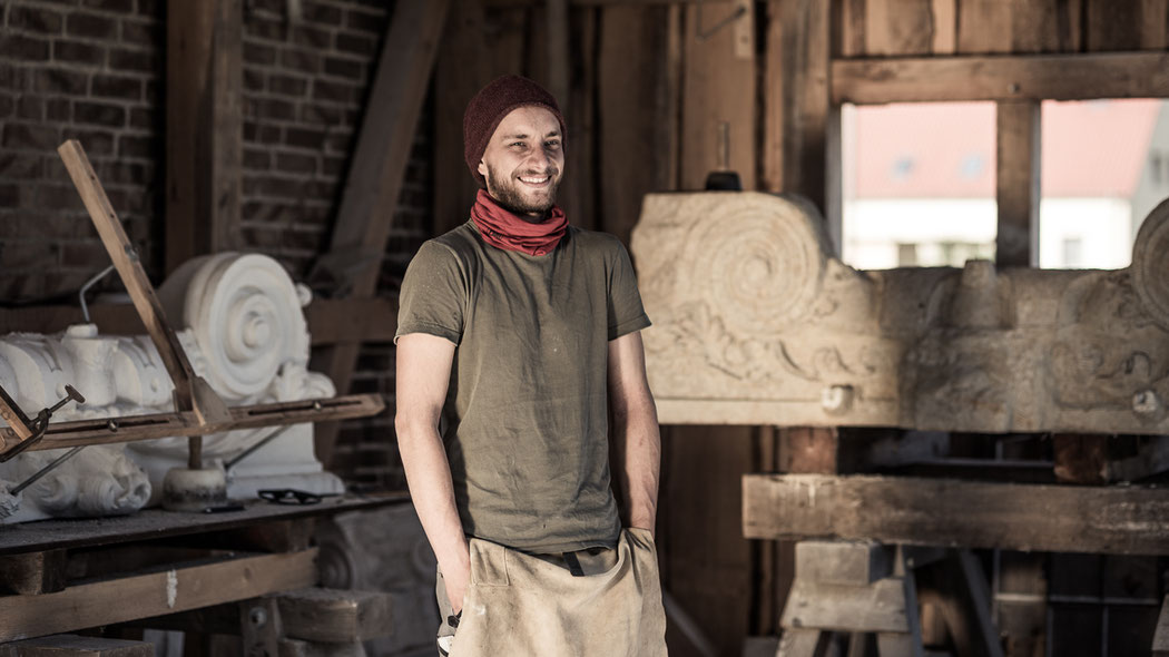 Steinmetz Marcus Scheffczyk steht in Zunftkleidung vor einem Bildhauer-Stück aus Sandstein
