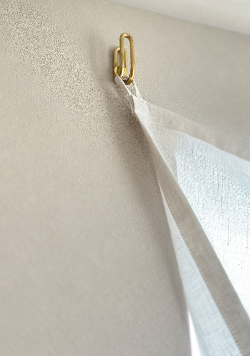 ふさかけに直接引っ掛けられるよう縫製されたリネンカーテン。金具に軽やかに掛かる様子