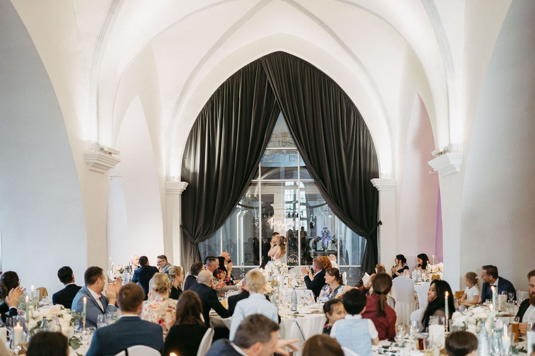 Feiernde Hochzeitsgesellschaft auf der Nonnenempore im Kloster Wöltingerode mit Blick in die Kirche. Hochzeitsfotografie Niedersachsen: Gäste stoßen nach der Rede auf das Brautpaar an.