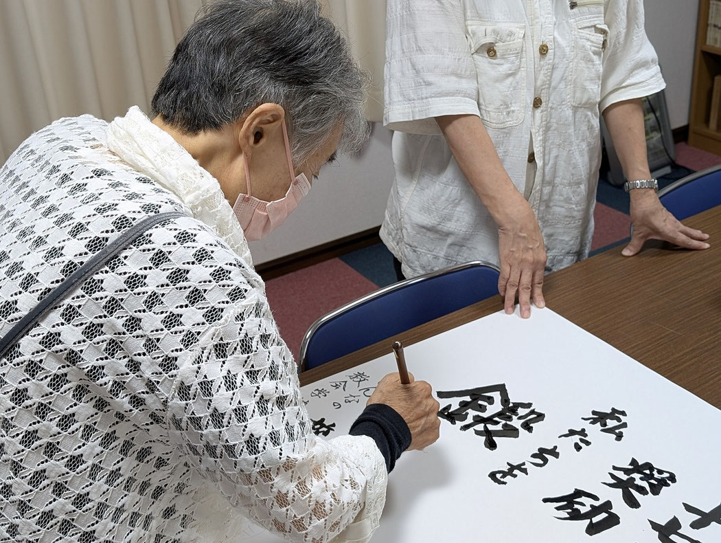 2025年8月10日(日)礼拝後 ほっとタイムというお茶と軽食の時間を終えた頃 教会堂の一番奥の部屋(コピー機があったり、小さな集会が行える部屋です)にて、次週礼拝案内を毛筆で書いておられるのが書子(ふみこ)さん。そして、助言をしつつ助け手として居られるのがりょうこさんです。貴いお働きに心から感謝!