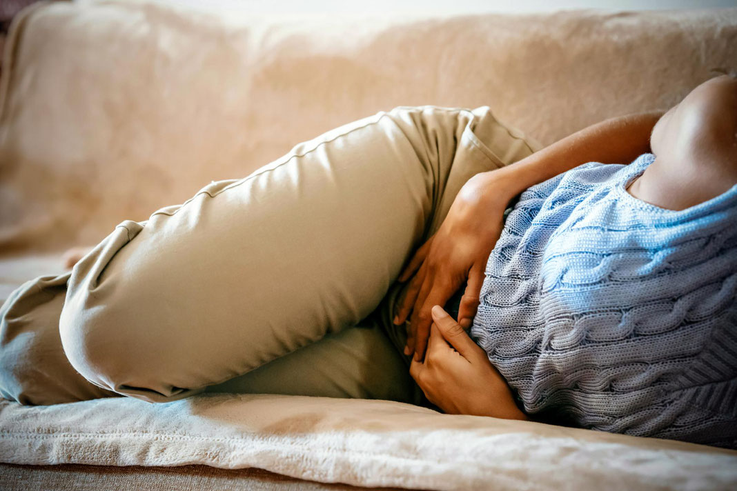 Frau krümmt sich vor Bauchschmerzen auf dem Sofa