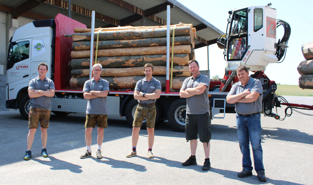 Das professionelle Team des Spitzensports Holztransport steht vor einem mit Rundholz beladen Holz-LKW
