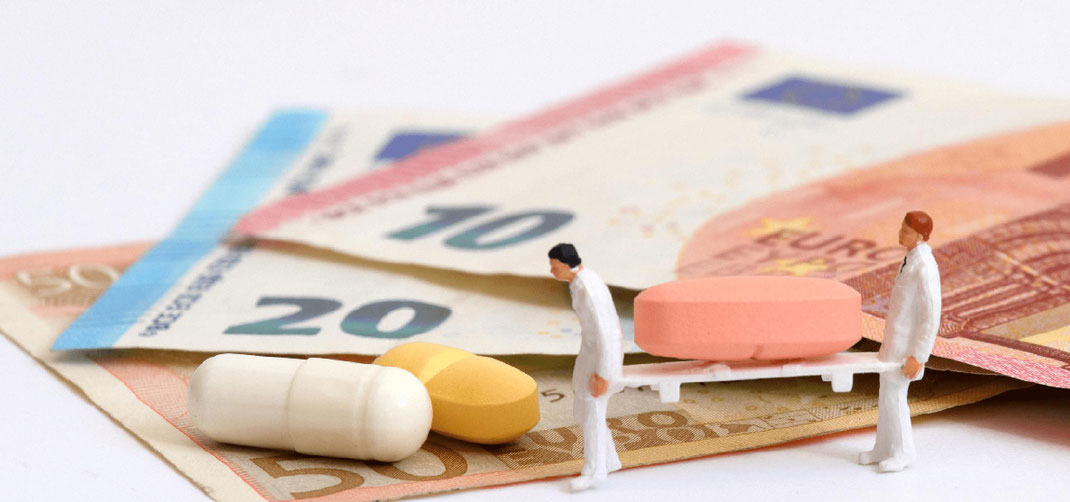 zwei mini figuren mit trage, darauf ligt eine pille und sie laufen über aufgefächerte euro-scheine