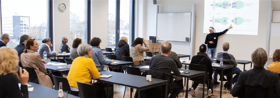 Ein Experte steht vor Publikum in einem PBV-Workshop vor einer Beamer-Präsentation