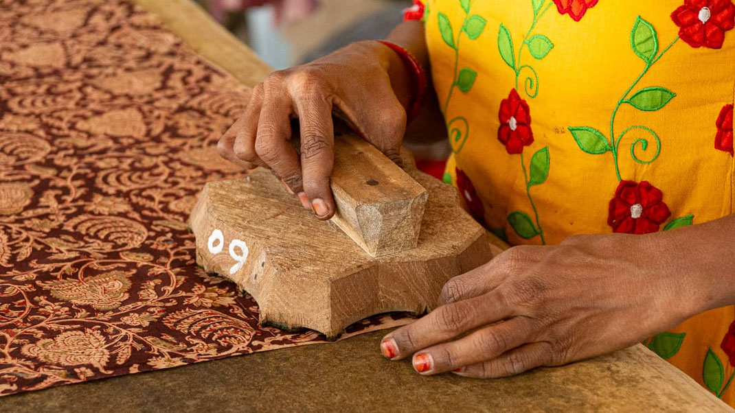 Un bloc de bois sculpté est appliqué sur un tissu déjà imprimé afin de lui ajouter une couleur supplémentaire.