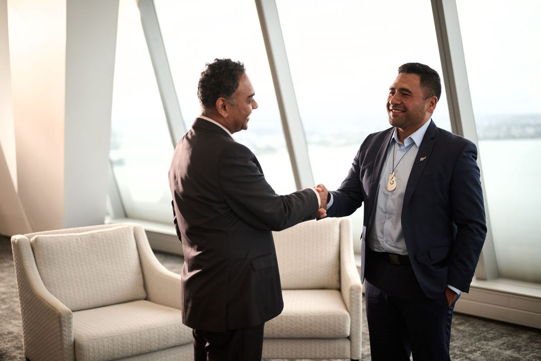 Deux hommes font affaire et se serrent la main debout dans un bureau confortable en Nouvelle-Zélande avec des fenêtre donnant sur la baie d'Auckland