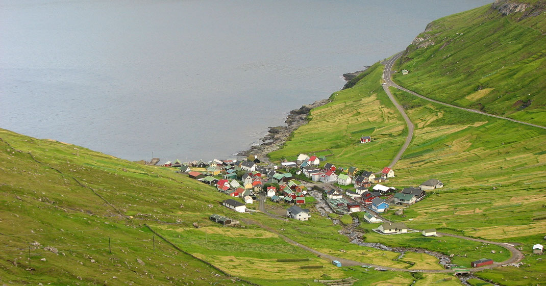 Sehenswürdigkeiten Funningur: Die bunten Häuser von Funningur wurden um einen kleinen Gebirgsbach, der in den Fjord mündet, gebaut. Gut geschützt stehen große Laubbäume zwischen den Häusern.