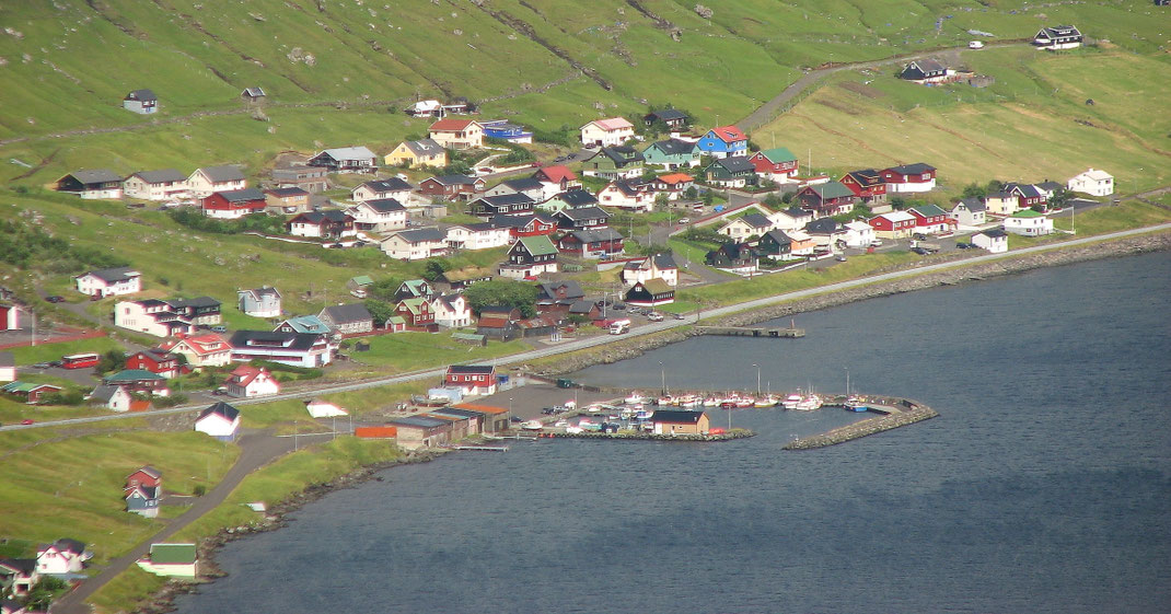 Sehenswürdigkeiten Streymoy: Die bunten Holzhäuser des Fischerdorfs Kollafjørður liegen eng aneinander gebaut am Fuß eines Hügels am Ufer des Kollafjørðurfjords.