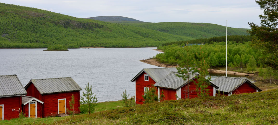Sehenswürdigkeiten Pappila (Utsjoki): Typische nordische Holzhäuser mit weißen Eckrändern stehen eng zueinander am Fluss.