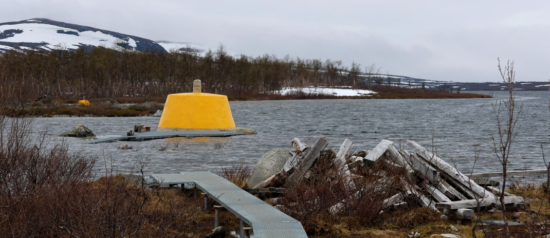 Sehenswürdigkeiten Kilpisjärvi - Dreiländereck: Zwei Grenzmarkierungen zeigen den Grenzverlauf zu Norwegen an. Im Vordergrund liegt ein Haufen mit Bretter, die für den früheren Holzweg genutzt worden war.