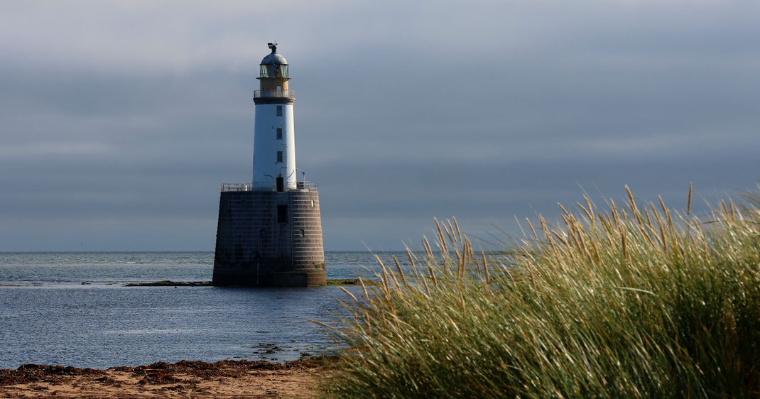 Sehenswürdigkeiten Rattray Head: Rattray Head Lighthouse mit dem imposanten Steinwerk-Sockel und dem für Leuchttürme typisch weißen Turm und dem oben abschliessenden Leuchtfeuer steht etwas vom Sandstrand entfernt im ufernahen Wasser der Nordsee.